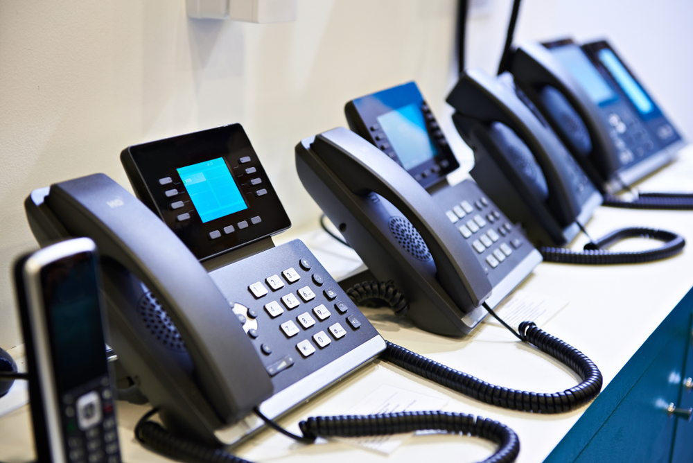 Row of modern VoIP desk phones with digital displays on a white office counter