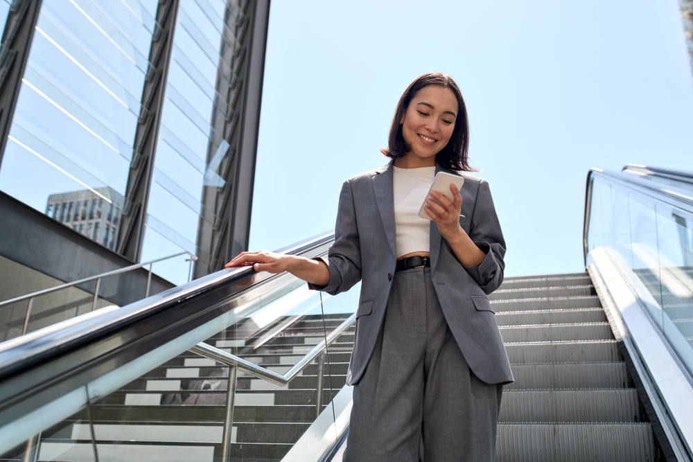 businesswoman standing on an urban escalator using applications on cell phone