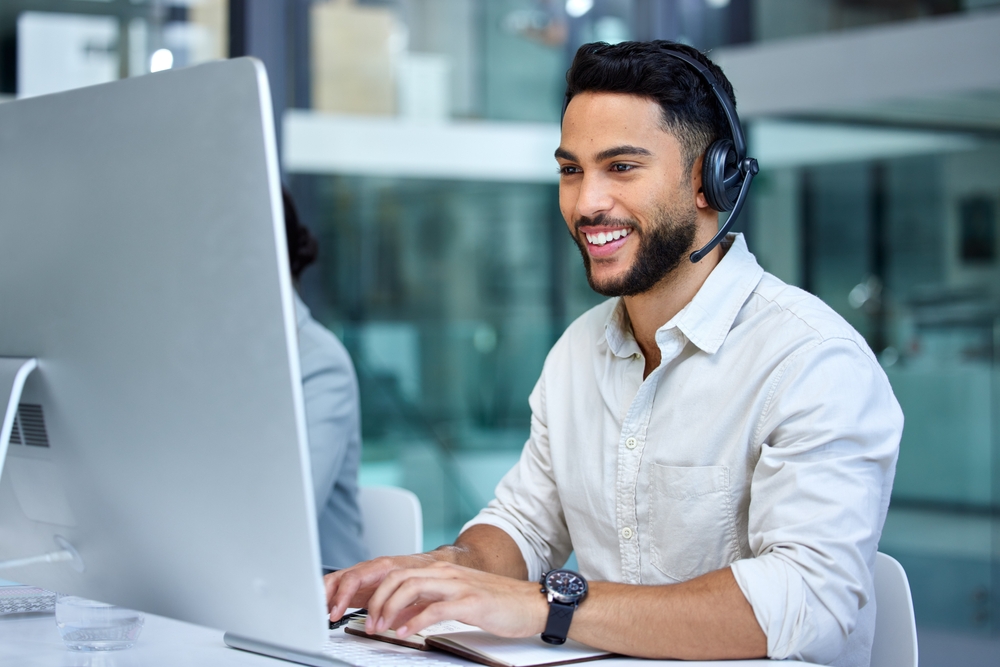 Smiling man wearing a headset working at a desktop computer in a modern office